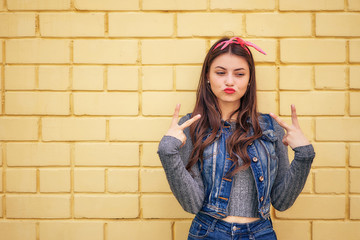 young woman in a denim suit with a pink bow emotionally fun posing on a background of a yellow brick wall. copy space