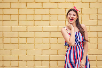 close-up young woman in a summer dress with a pink bow emotionally fun posing on a background of a yellow brick wall. copy space