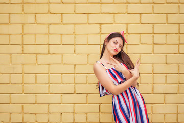close-up young woman in a summer dress with a pink bow emotionally fun posing on a background of a yellow brick wall. copy space
