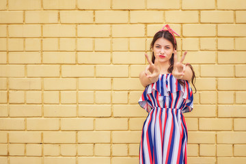 close-up young woman in a summer dress with a pink bow emotionally fun posing on a background of a yellow brick wall. copy space