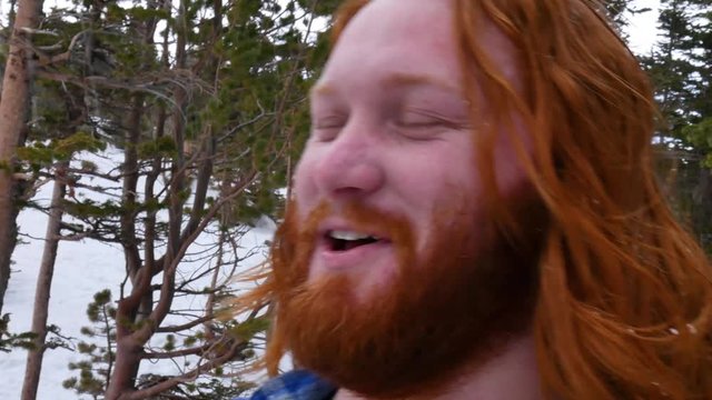 Long haired redhead bearded caucasian male in the snow having fun looking at camera, handheld