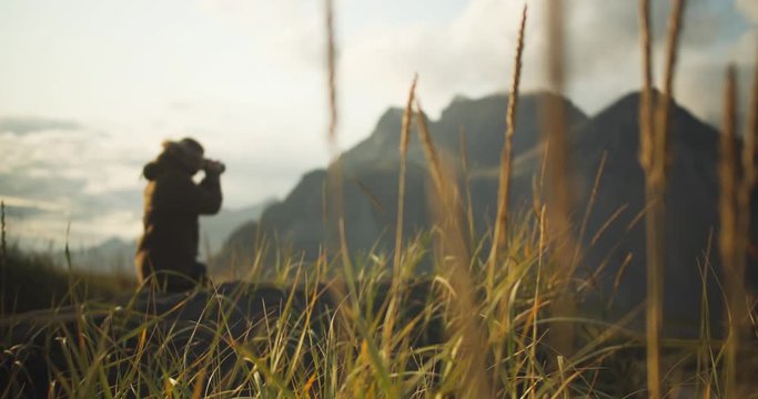 Focus shift to young hiker kneeling in hilly northern landscape taking pictures