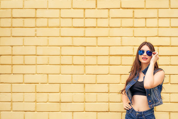 cheerful hipster girl going crazy making funny face and showing her tongue. yellow urban wall background. copy space