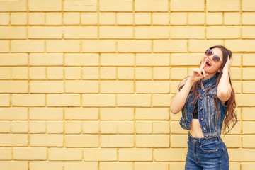 Fototapeta na wymiar Hipster girl emotionally posing on a background of yellow brick wall. copy space
