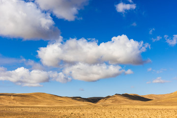Clouds on a blue sky over mountains with dried yellow grass