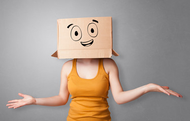 Young woman standing and gesturing with a cardboard box on her head with drawn smiley face