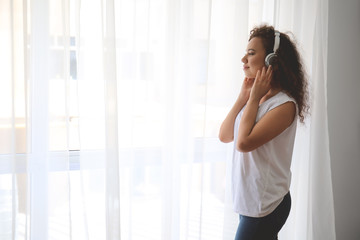 Beautiful young woman listening to music near window at home