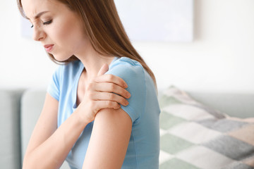 Young woman suffering from pain in shoulder at home