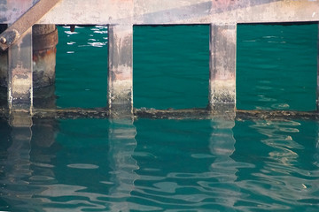 The berth supports are reflected on the surface of the water. Waves and glare of light and beautiful color.