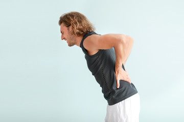 Young man suffering from back pain on color background