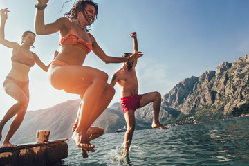 Group of friends jumping off the pier into the sea. Selective focus