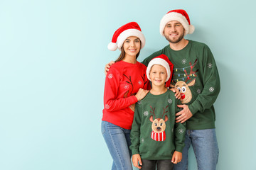 Happy family in Christmas sweaters and Santa hats on color background