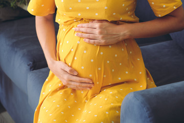 Beautiful pregnant woman sitting on sofa, closeup