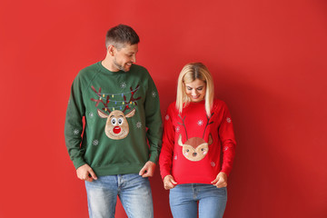 Happy couple in Christmas sweaters on color background