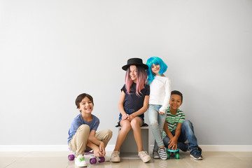 Stylish little children with skateboards near light wall