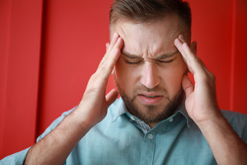 Young man suffering from headache on color background