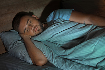 Fototapeta na wymiar Young man sleeping in bed at night