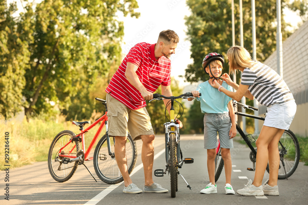 Poster Parents teaching their son to ride bicycle outdoors