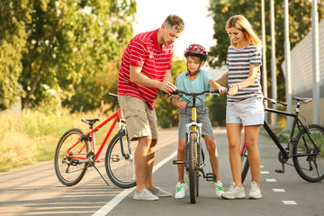Parents teaching their son to ride bicycle outdoors