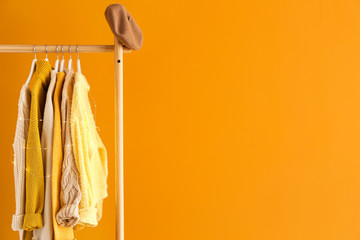 Rack with winter clothes on color background