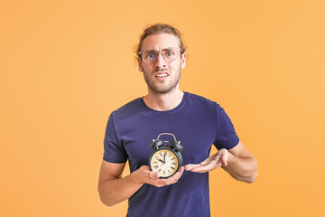Stressed man with alarm clock on color background