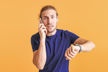 Stressed man talking by phone while looking at watch on color background