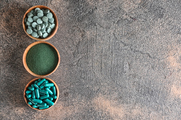 Bowls with spirulina powder and pills on grey background