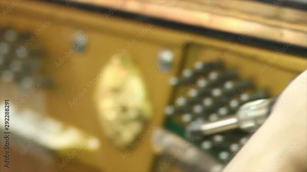 Poster view from behind of a person listening to and tuning a piano by hand.