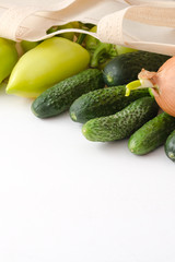 Onion, cucumber, zucchini, pepper in eco bag on white wooden background.