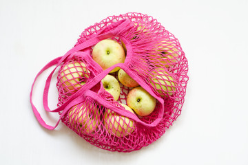 Pink mesh shopping bag with fresh apples on white background