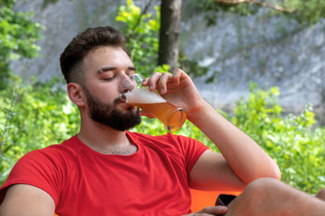 young bearded man or guy drinks beer from a glass outdoors. at the picnic enjoys relaxation. Tourism and summer camping concept