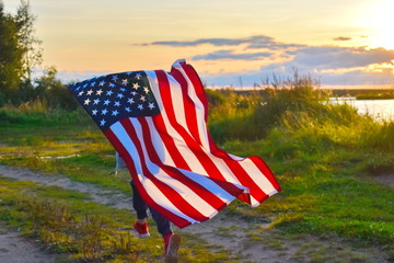 A child runs with the American flag at sunset.