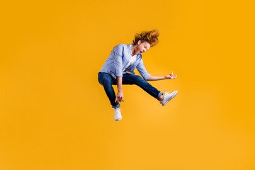 Fototapeta na wymiar Full length body size photo of crazy red haired rock playing guy musician fan wearing jeans denim checkered blue shirt sneakers pretending to play guitar jumping isolated vivid color background