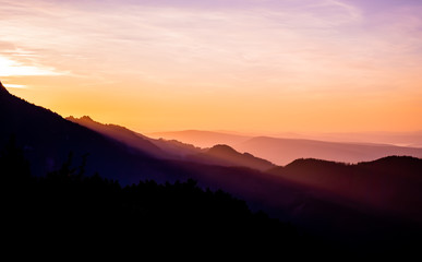 Romantic purple and orange sunset over the high Tatra mountains with dense mist and long sun rays