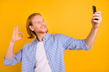 Photo of cheerful cute nice fun positive funky man blogger talking video call smiling toothily wearing checkered blue shirt taking selfie isolated over bright color yellow background