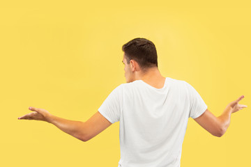 Caucasian young man's half-length portrait on yellow studio background. Beautiful male model in shirt. Concept of human emotions, facial expression, sales, ad. Showing and pointing something.