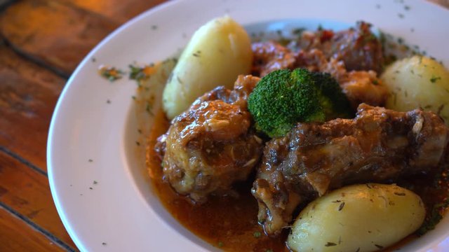 traditional spanish dish, slow cooked oxtail in wine sauce with baked potatoes and broccoli, slow panning footage in 4k, holiday food in andalucia, spain