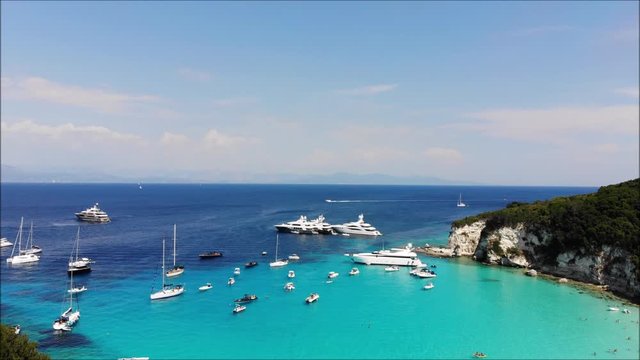 Reveal shot of a Greek bay with stunning blue water and superyachts. Filmed by drone