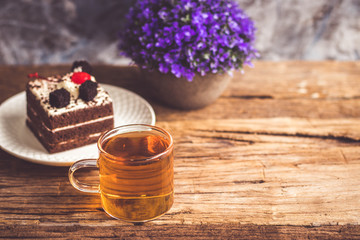 Obraz na płótnie Canvas Hot tea In clear glass, black forest creek cake decorate with cherry and cake brownies In a white plate, and have false heather In pots small, all place are on wooden table.