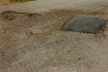 Fototapeta na wymiar Damaged road, cracked asphalt. Asphalt with potholes and spot. Very bad asphalt road with large cracks. Scary technology in road construction. Numerous dangerous failures patching of road