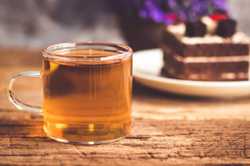 Hot tea In clear glass, black forest creek cake decorate with cherry and cake brownies In a white plate, and have false heather In pots small, all place are on wooden table.