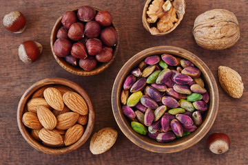 Various nuts in wooden bowls on dark wood background . Almond , pistachio and hazelnut. Top view