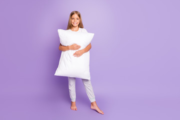 Full length photo of positive cheerful content kid hug hold carry pillow feel dreamy wakeup in morning wear white t-shirt pajama pants isolated over violet purple color background