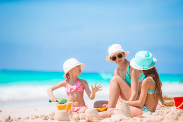 Mother and little daughters making sand castle at tropical beach