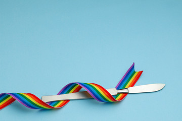 Scalpel and rainbow LGBT ribbon pride symbol. Sex change operation. Blue background. Copy space for text.