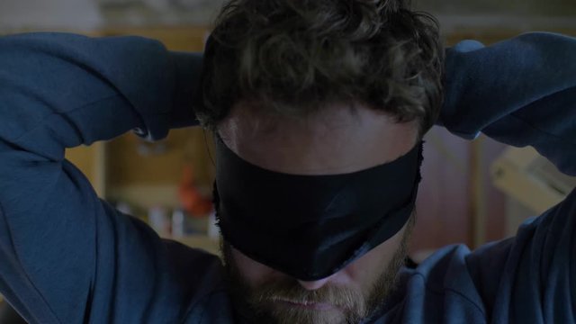 A Man With A Beard Is Tying A Black Blindfold Over His Eyes. Blindfolded Man.Terrorism. . 4k. 4k video. 60 fps