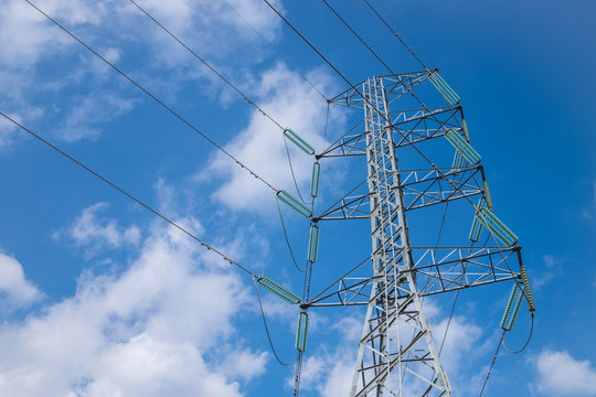 High voltage pole and high voltage cables with cloud and blue sky background.
