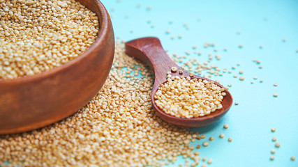 White quinoa seeds on a blue background. quinoa in bowl and a spoon on kitchen table top view. Healthy and diet superfood product.