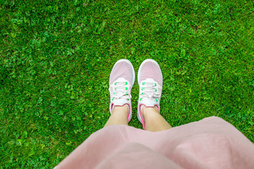 Legs in pink sneakers on green grass.