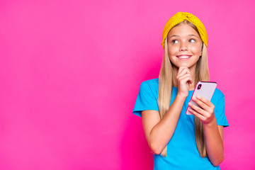 Hmm... What write on blog. Portrait of lovely funky positive child use her cellphone read feedback think what to post wear yellow headband blue t-shirt isolated over pink color background